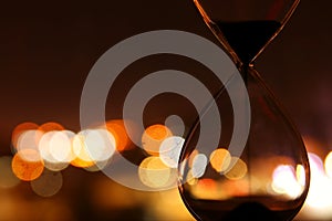 Hourglass over bokeh city lights as time passing concept for business deadline.