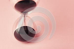 Hourglass on pink background, closeup. Urgency and running out of time concept