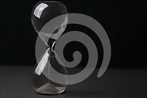 Hourglass with sand falling through, set against a black backdrop, the concept of time passing