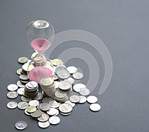 Hourglass with sand flowing and coins on table