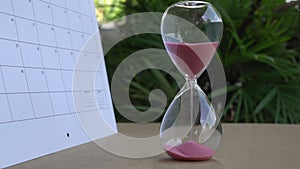 Hourglass with sand flowing, next to calendar. Time passing.