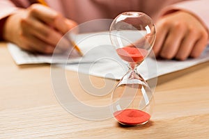 Hourglass with time running out and student hand testing in exercise and passing exam carbon paper computer sheet with pencil in