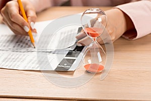 Hourglass with time running out and student hand testing in exercise and passing exam carbon paper computer sheet with pencil in