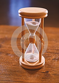 Hourglass on wooden table, dark background. Sand falling down inside of hourglass. Time flow concept. Wooden hourglass