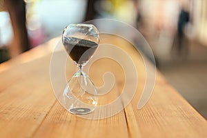 Hourglass on wooden table outdoors in the rays of sunlight. Business deadline concept