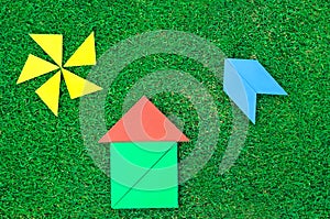 House, aircraft and sun made of tangram figures on natural grass