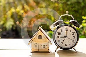 The house and alarm clock stack on wood table and sunset background in the public pack and Business concept.