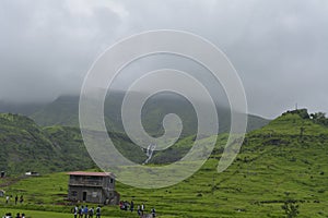 House around tourists with green mountains river flowing under fogy clouds in Ashane, India