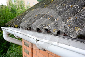 House asbestos roof with close up gutter holder and plastic roof gutter pipe. Guttering