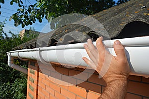 House asbestos roof with plastic roof gutter pipe repair. Contractor hand repair house roof gutter photo