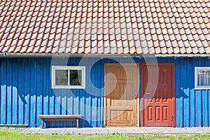 House of blue wooden planks, red roof, two colorful doors and small windows