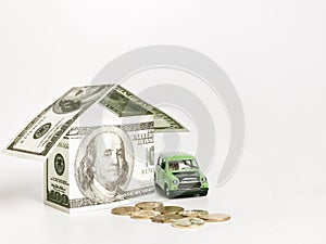 House built of banknotes with coins and toy car against white background.