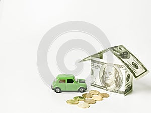 House built of banknotes with coins and toy car against white background.