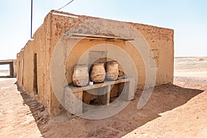 House built of mud bricks in the desert with a bench on which drinking clay jugs with water are standing ready photo