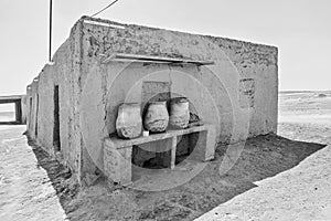 House built of mud bricks in the desert with a bench on which drinking clay jugs with water are standing ready, Sudan, black and photo