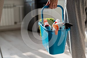 House cleaning concept. Faceless woman holds cleaning products in a blue basket. Closeup of the hands of a female