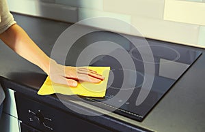 House cleaning concept - woman holding dry microfiber rag wiping the glass surface induction cooker and kitchen countertop from