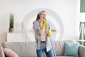 House cleaning is fun. Cheerful young lady using mop as mic, singing song while doing cleanup at living room