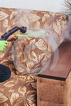 House cleaning. A girl in green gloves cleans the sofa and furniture with a steam generator. we kill microbes. Cleaning service of