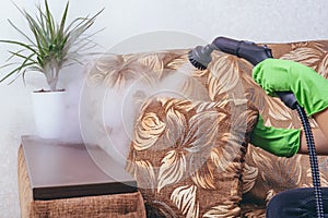 House cleaning. A girl in green gloves cleans the sofa and furniture with a steam generator. we kill microbes. Cleaning service of