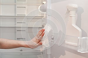 House cleaning - spray bottle with detergents for washing the fridge. The housekeeper wipes the shelves of a clean refrigerator wi photo