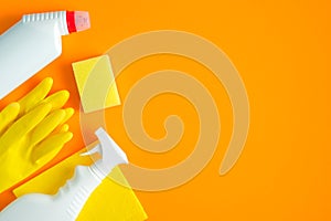 House cleaning supplies and cleaning products on orange background. Top view yellow sponge, napkin and rubber gloves with cleaner