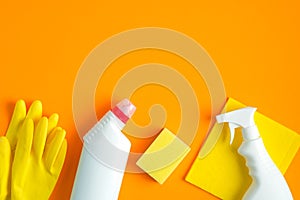 House cleaning supplies and cleaning products on orange background. Top view yellow sponge, napkin and rubber gloves with cleaner