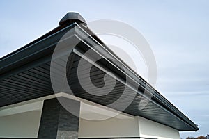 House corner with brown metal planks siding and roof with steel gutter rain system. Roofing, construction, drainage