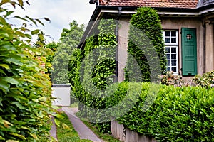 A house covered with green plants next to a driveway and a white garage in a backyard in Germany