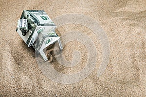 House cut out of dollar bills on the sand