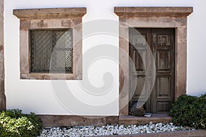 House exterior door and window. White and brown colors. old pots in front of the door. It was pulled through the street