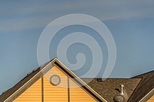 House exterior with roof shingles and round gable window against blue sky