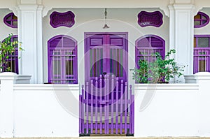 house exterior with white walls and purple windows, door and fence. cozy house is behind fence.