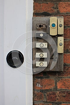 House front with 7 modern analog doorbells attached to a old worn wooden piece of wood