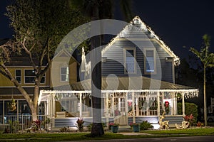 House front yard with big porch brightly illuminated with christmas decorations. Outside decor of florida family home