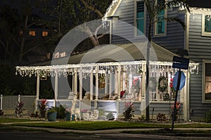 House front yard with big porch brightly illuminated with christmas decorations. Outside decor of florida family home