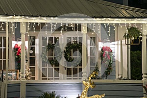 House front yard with big porch brightly illuminated with christmas decorations. Outside decor of florida family home