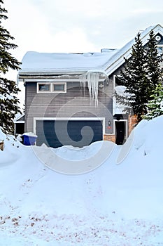 House with gray garage door against snowy driveway yard and roof in winter