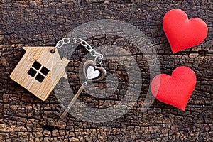 House key in heart shape with home keyring on old wood background decorated with mini heart