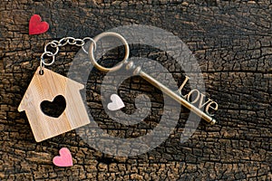 House key in heart shape with home keyring on old wood background decorated with mini heart