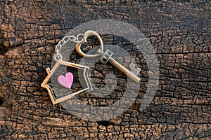 House key in heart shape with home keyring on old wood background decorated with mini heart