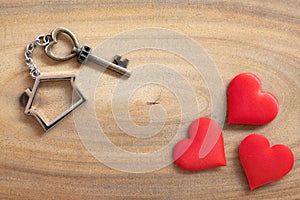 House key in heart shape with home keyring on old wood background decorated with mini heart