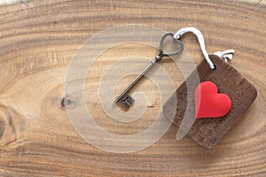 House key in heart shape with home keyring on old wood background decorated with mini heart