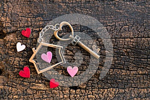 House key in heart shape with home keyring on old wood background decorated with mini heart