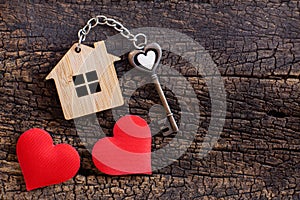 House key in heart shape with home keyring on old wood background decorated with mini heart