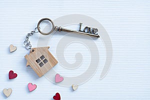 House key in heart shape with home keyring on old wood background decorated with mini heart