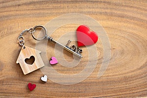 House key in heart shape with home keyring on old wood background decorated with mini heart