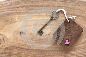 House key in heart shape with home keyring on old wood background decorated with mini heart