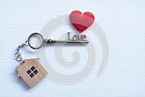 House key in heart shape with home keyring on white wood background decorated with mini heart