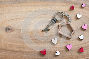 House key in heart shape with home keyring on wood background decorated with mini hearts